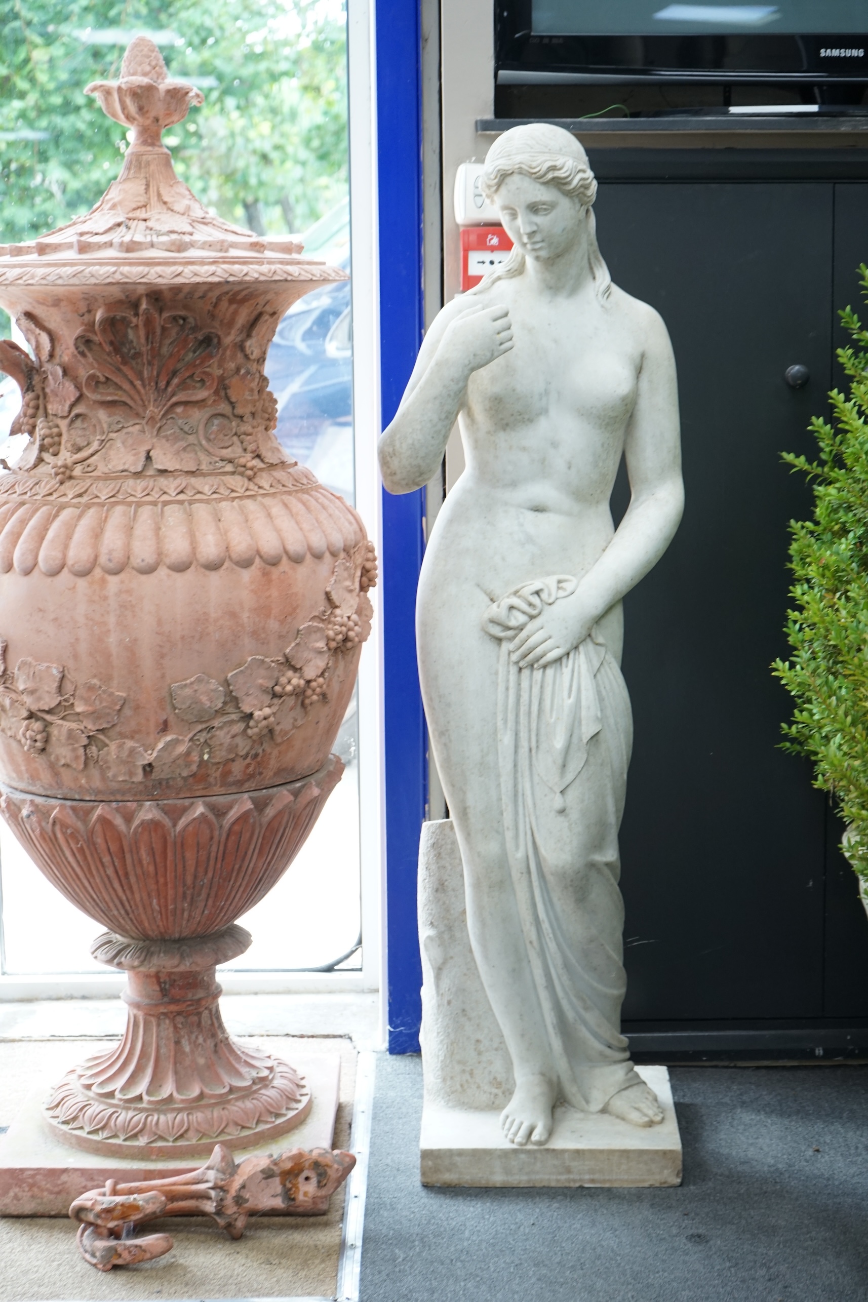 After the Antique. A large carved reconstituted marble figure of Venus, standing beside a tree trunk, 141cm high